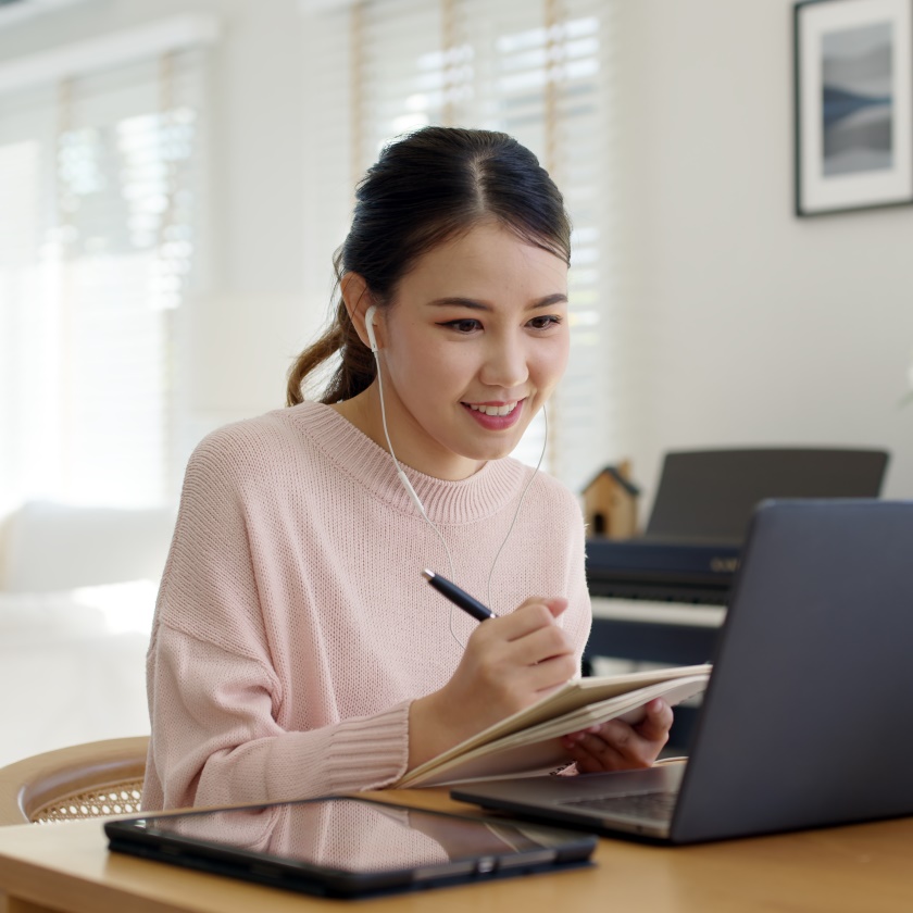 Female employee wearing earphone listening to digital online course.